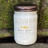 Jar of Hattie Hazel candle on a stone surface with greenery in the background