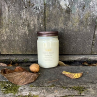 soy candle in clear jar with metal lid with leaves and walnuts scattered about